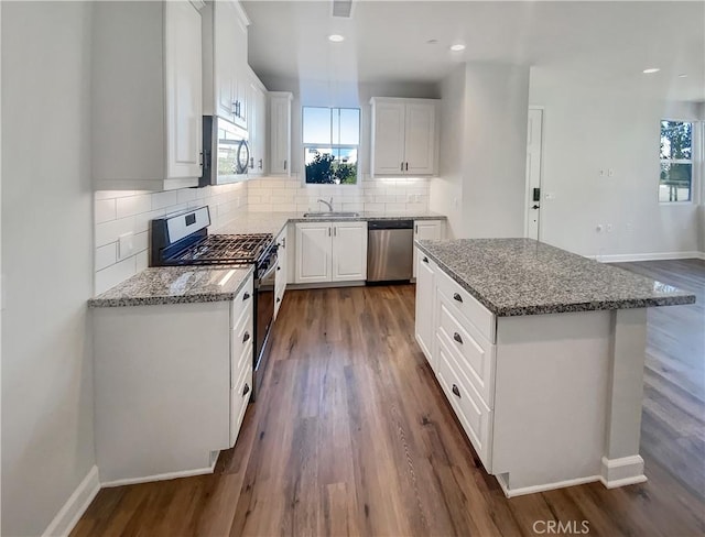 kitchen featuring white cabinetry, stainless steel appliances, a center island, and light stone counters