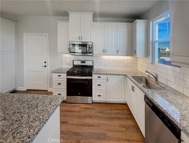 kitchen featuring appliances with stainless steel finishes, white cabinetry, sink, light hardwood / wood-style floors, and light stone countertops