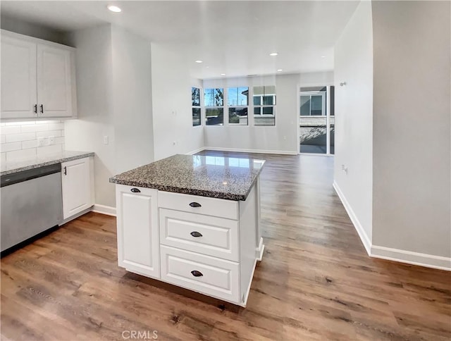 kitchen with white cabinetry, stainless steel dishwasher, dark stone counters, hardwood / wood-style floors, and decorative backsplash