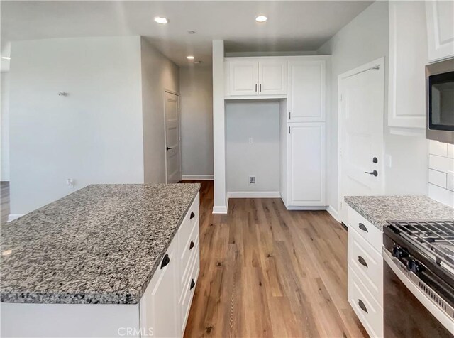 kitchen with white cabinetry, stone countertops, a kitchen island, and light wood-type flooring