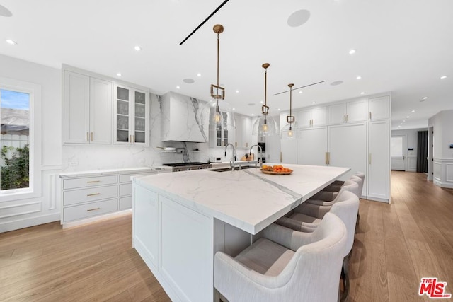 kitchen with pendant lighting, white cabinetry, a kitchen island with sink, light stone counters, and a kitchen bar