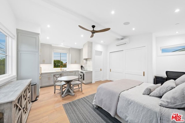 bedroom with sink, vaulted ceiling with beams, a wall unit AC, ceiling fan, and light hardwood / wood-style floors