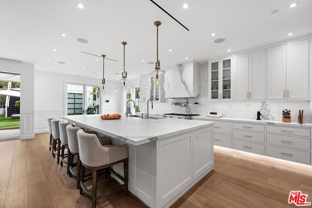 kitchen featuring white cabinets, a kitchen breakfast bar, a large island with sink, hanging light fixtures, and light hardwood / wood-style flooring