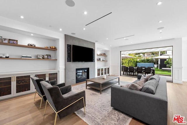 living room with built in shelves, a large fireplace, and light hardwood / wood-style floors