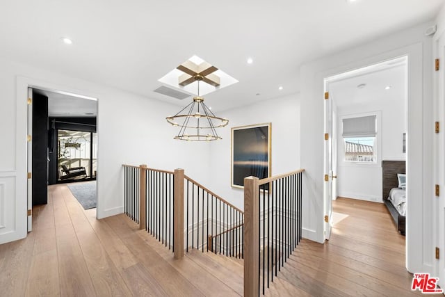 hallway featuring an inviting chandelier, a wealth of natural light, and light hardwood / wood-style floors