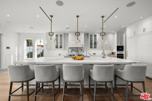 kitchen featuring a large island with sink, hanging light fixtures, a breakfast bar, and white cabinets