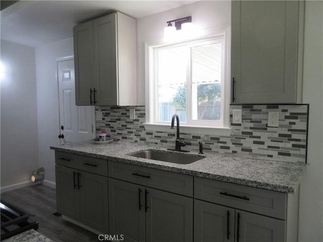 kitchen featuring sink, gray cabinetry, light stone counters, dark hardwood / wood-style floors, and decorative backsplash