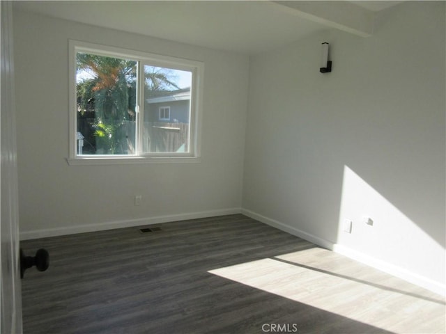 empty room featuring beamed ceiling and dark hardwood / wood-style floors