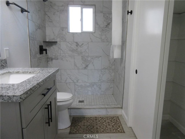 bathroom featuring toilet, tile walls, a tile shower, vanity, and tile patterned flooring