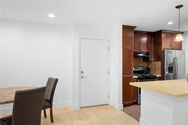 kitchen featuring tasteful backsplash, stainless steel appliances, decorative light fixtures, and light wood-type flooring