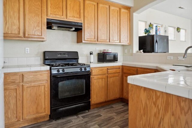 kitchen featuring dark hardwood / wood-style floors, tile countertops, sink, and black appliances