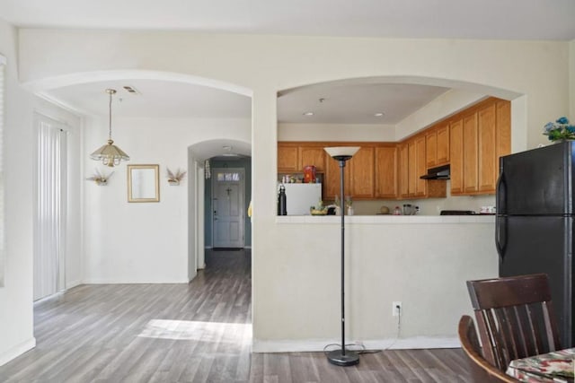 kitchen featuring refrigerator, black fridge, decorative light fixtures, exhaust hood, and light wood-type flooring