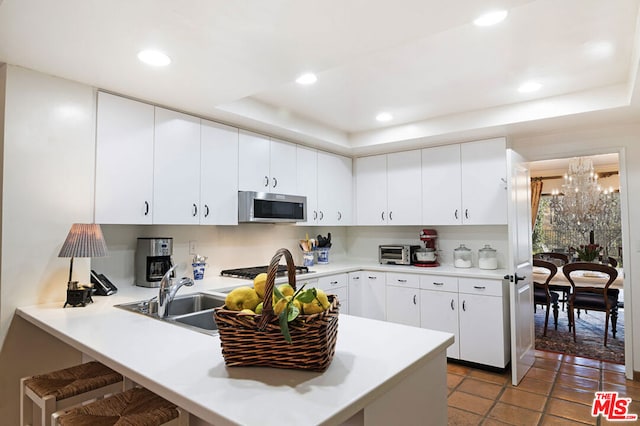 kitchen featuring white cabinetry, sink, a kitchen breakfast bar, kitchen peninsula, and a raised ceiling