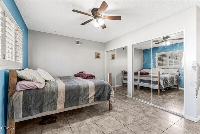 tiled bedroom featuring multiple closets, ceiling fan, and a textured ceiling