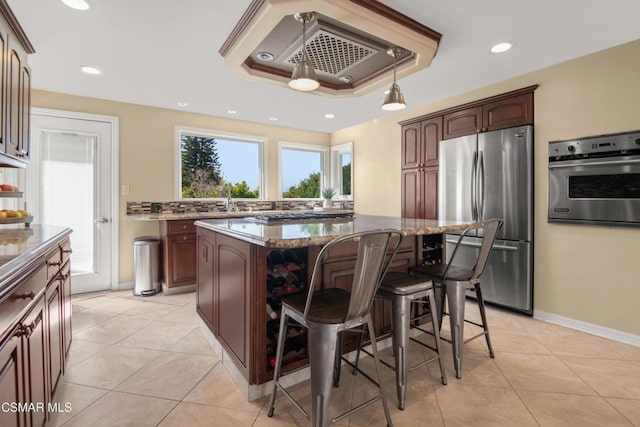 kitchen featuring light tile patterned floors, appliances with stainless steel finishes, a raised ceiling, a kitchen island, and dark stone counters