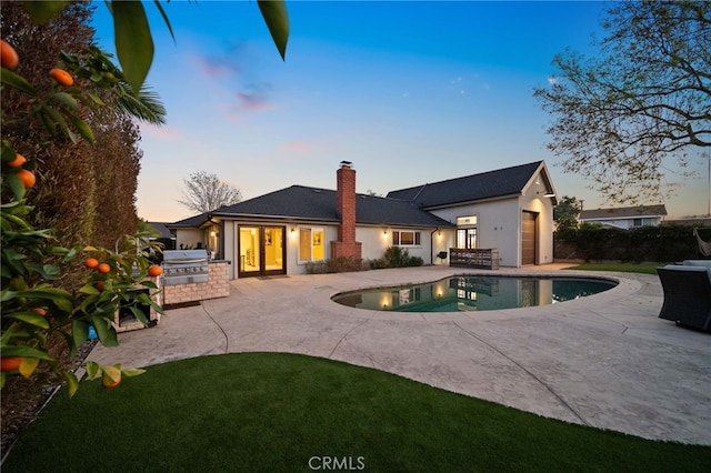 back house at dusk with a fenced in pool, exterior kitchen, and a patio