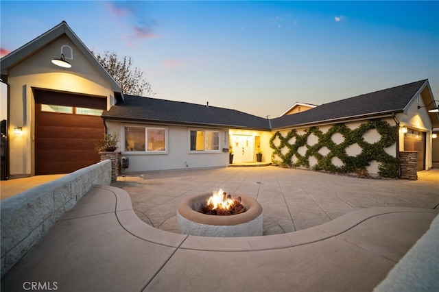 back house at dusk featuring a garage and an outdoor fire pit