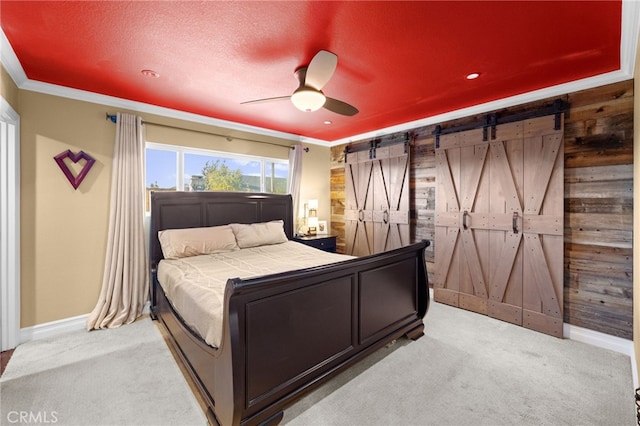 bedroom featuring ceiling fan, ornamental molding, light carpet, a barn door, and wood walls