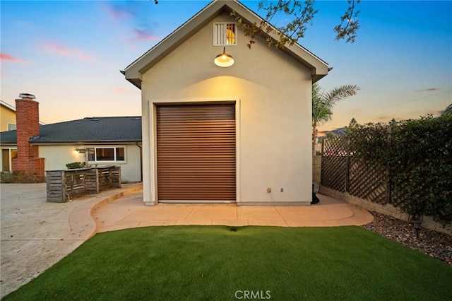 garage at dusk featuring a lawn