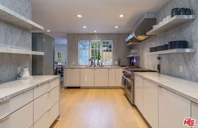 kitchen featuring white cabinetry, double oven range, light stone countertops, wall chimney range hood, and light wood-type flooring