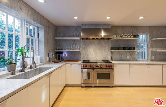 kitchen with wall chimney exhaust hood, sink, light stone counters, double oven range, and white cabinets