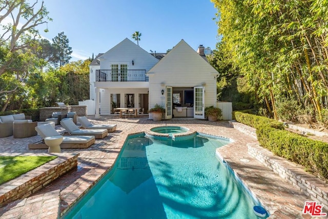 back of house with a balcony, an outdoor hangout area, a pool with hot tub, and a patio