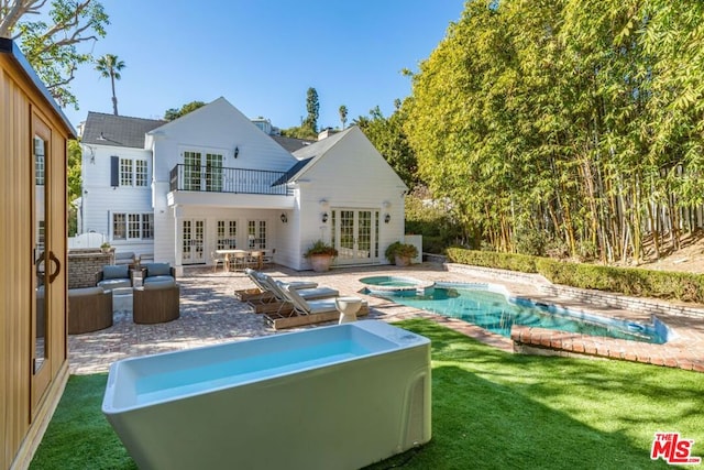 back of house featuring a patio, an outdoor living space, a pool with hot tub, french doors, and a balcony