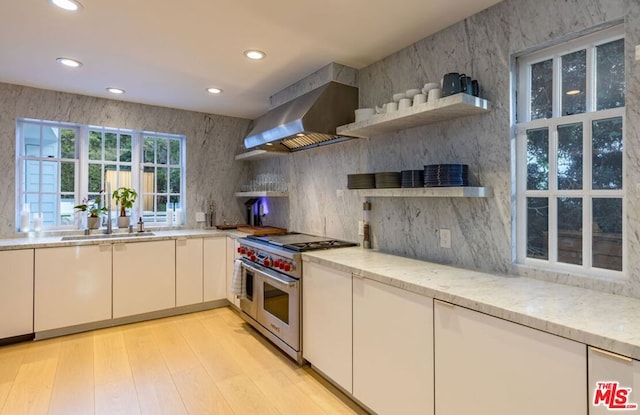 kitchen with white cabinetry, double oven range, light stone countertops, light hardwood / wood-style floors, and wall chimney range hood