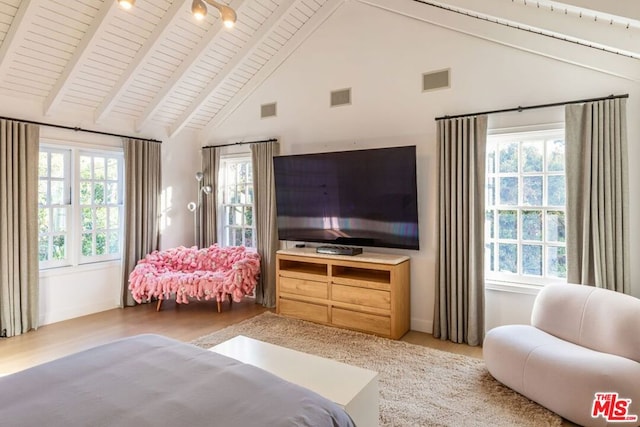 bedroom featuring vaulted ceiling with beams, multiple windows, and light wood-type flooring