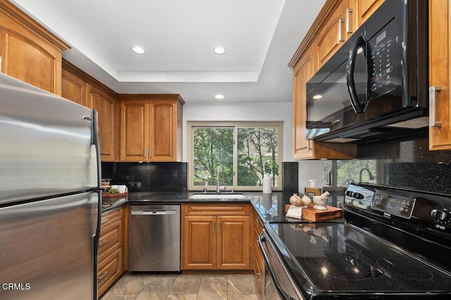 kitchen with sink, black appliances, dark stone countertops, a raised ceiling, and backsplash