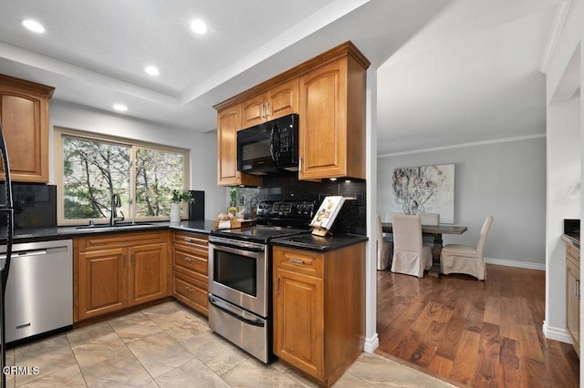 kitchen with sink, appliances with stainless steel finishes, dark stone counters, light hardwood / wood-style floors, and decorative backsplash