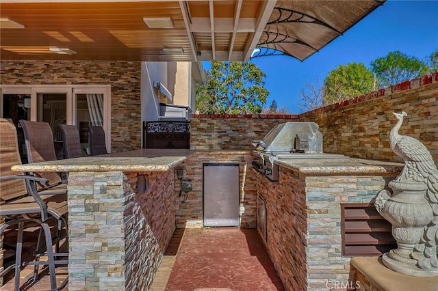 view of patio featuring exterior bar, a grill, and an outdoor kitchen