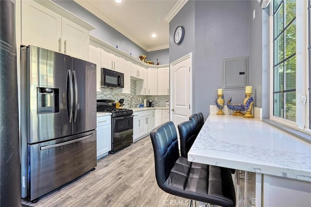 kitchen featuring ornamental molding, black appliances, a kitchen breakfast bar, and white cabinets