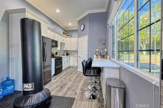 kitchen featuring white cabinets, decorative backsplash, black appliances, crown molding, and light hardwood / wood-style flooring