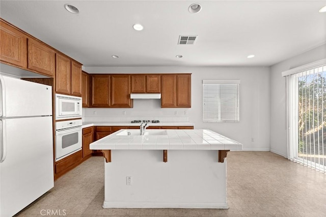 kitchen featuring sink, white appliances, a breakfast bar, tile counters, and a center island with sink