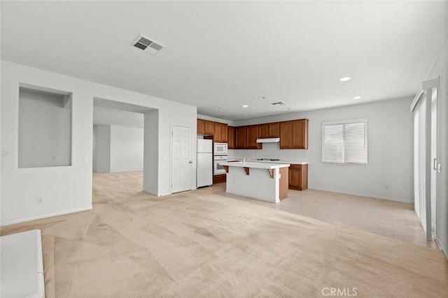 kitchen with light carpet, white appliances, a breakfast bar area, and a center island