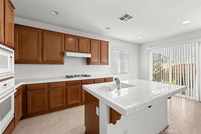 kitchen with white appliances, sink, tile countertops, and a kitchen island with sink