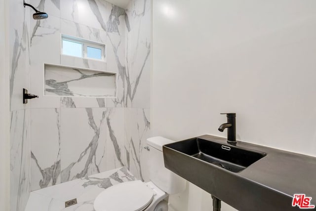 bathroom with sink, a tile shower, and toilet