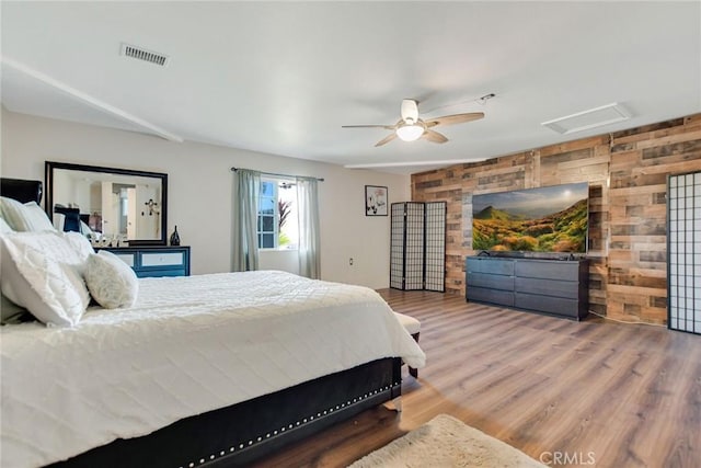 bedroom with visible vents, wood finished floors, wood walls, attic access, and ceiling fan