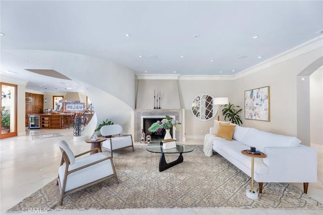 living room with arched walkways, wine cooler, a premium fireplace, stairway, and crown molding