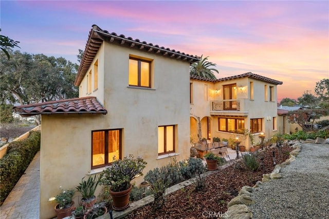 back house at dusk with a balcony and a patio