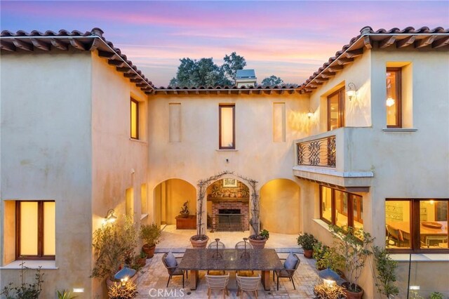 back house at dusk with a patio and an outdoor fireplace