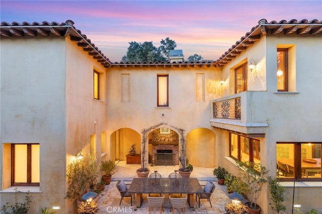 rear view of house featuring a balcony, a patio area, an outdoor brick fireplace, and stucco siding