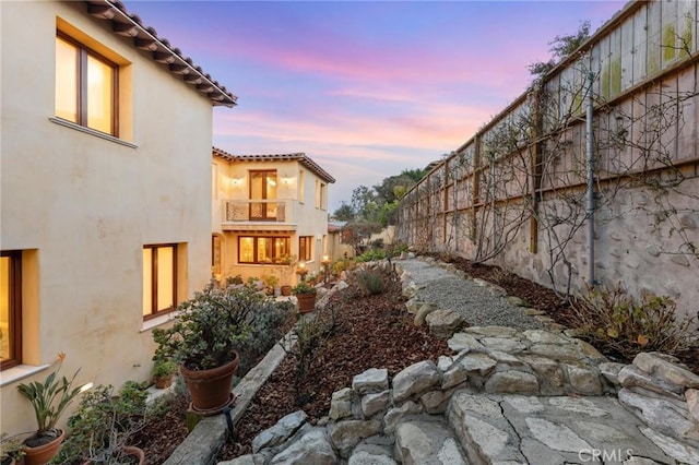 yard at dusk featuring a fenced backyard and a balcony