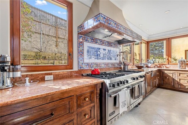 kitchen with range with two ovens, premium range hood, light stone countertops, and light tile patterned floors