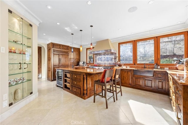 kitchen featuring decorative light fixtures, sink, a breakfast bar area, custom range hood, and a center island with sink