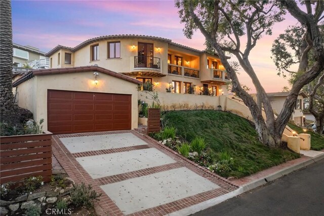 mediterranean / spanish-style house with a garage, concrete driveway, a balcony, a tile roof, and stucco siding