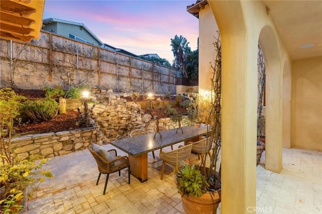 patio terrace at dusk featuring outdoor dining space and fence