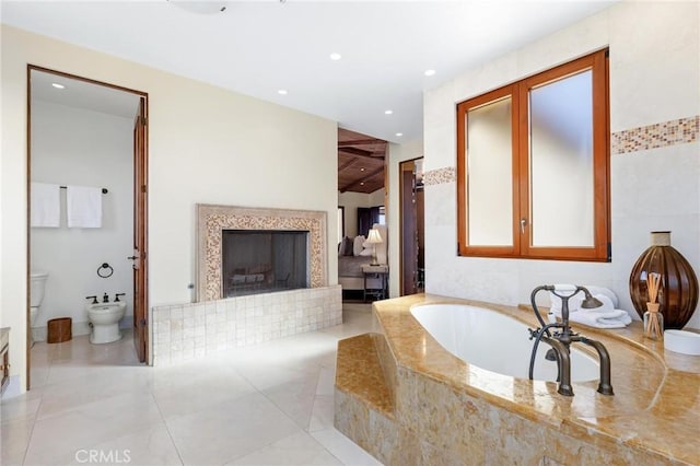 bathroom with a bidet, tiled bath, and toilet