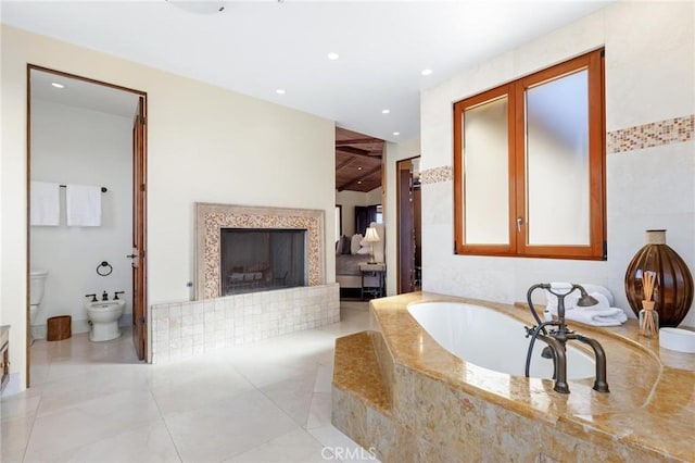 ensuite bathroom featuring recessed lighting, a fireplace with raised hearth, ensuite bathroom, a bidet, and a bath